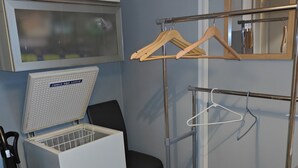 Habitación pequeña con un electrodoméstico blanco, una silla, una percha metálica y un espejo.