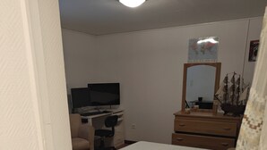 Un dormitorio con cama, escritorio con computadora, silla, cómoda y espejo.