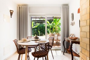 A dining area with a round table, chairs, and a view of the garden through a glass door. - Andorinha OCV | Peaceful Retreat, Pool & Garden (Albufeira)