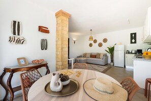 A modern living room with a dining area, kitchen, and a brick column. - Andorinha OCV | Peaceful Retreat, Pool & Garden (Albufeira)