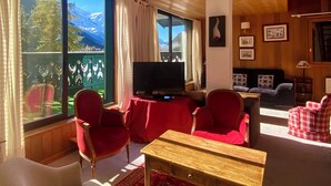 Uma sala de estar aconchegante com televisão, poltronas vermelhas, uma mesa de madeira e um sofá.