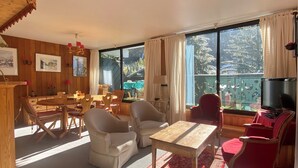 Uma sala de estar aconchegante com área de jantar, paredes de madeira e janelas grandes com vista para árvores cobertas de neve.