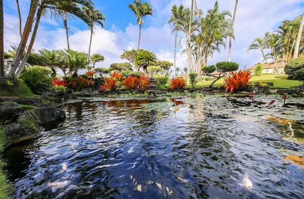 A tranquil water feature with a stone bridge, surrounded by lush tropical vegetation and palm trees.