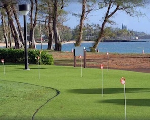 A golf course with a water body in the background, surrounded by trees and a clear sky.