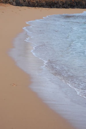 A sandy beach with gentle waves and a rocky shoreline.