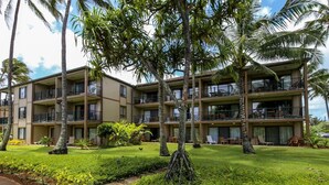 A multi-story hotel with balconies, a well-maintained lawn, and palm trees.