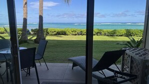 A patio with a view of the ocean, a lawn, and a table with chairs.