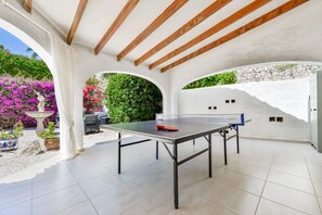 Ein Pingpongtisch in einem überdachten Außenbereich mit weißen Wänden, Holzbalken und einer Steinwand.