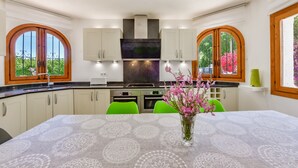 A modern kitchen with white cabinets, a black range hood, and a dining area with a table and chairs. - Villa rental in Moraira PONENT (Moraira)