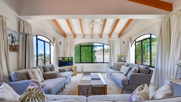 A spacious living room with two sofas, a coffee table, and a TV. Large windows offer a view of greenery outside. - Villa rental in Moraira PONENT (Moraira)