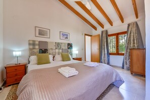 Ein Schlafzimmer mit Bett, Nachttischen, einem Holzkopfteil, einem Fenster mit Vorhängen und einem Holzschrank.