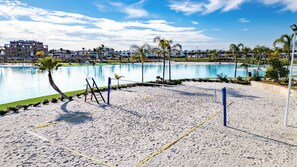 Una cancha de voleibol de playa con red, palmeras y una piscina al fondo.