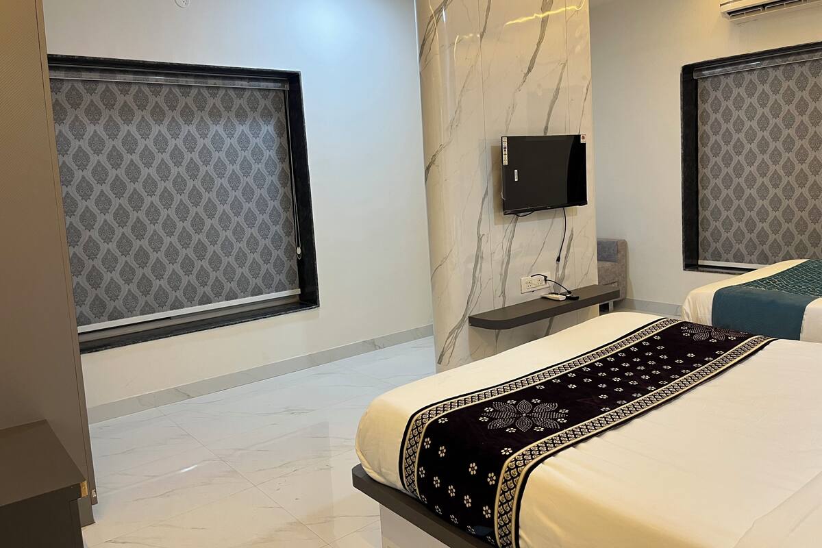 Une chambre d’hôtel moderne avec un mur en marbre, un téléviseur à écran plat, une table de chevet et un lit recouvert d’une couvre-lit à motifs.