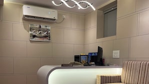 A reception desk with a 'RECEPTION' sign, a modern light fixture, an air conditioning unit, and a patterned rug. - Hotel Legacy Inn (Nagpur)