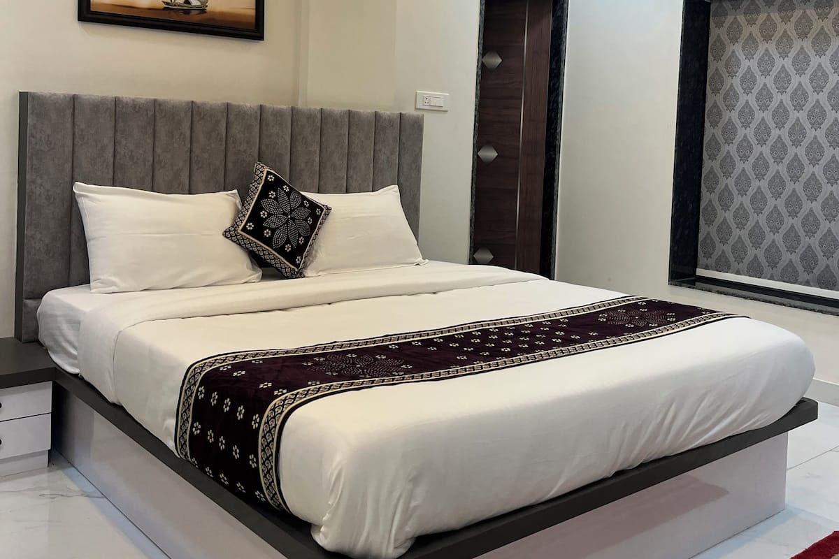 Une chambre moderne avec un grand lit, un ventilateur de plafond, un appareil de climatisation, une œuvre d’art encadrée et un mur à motifs.