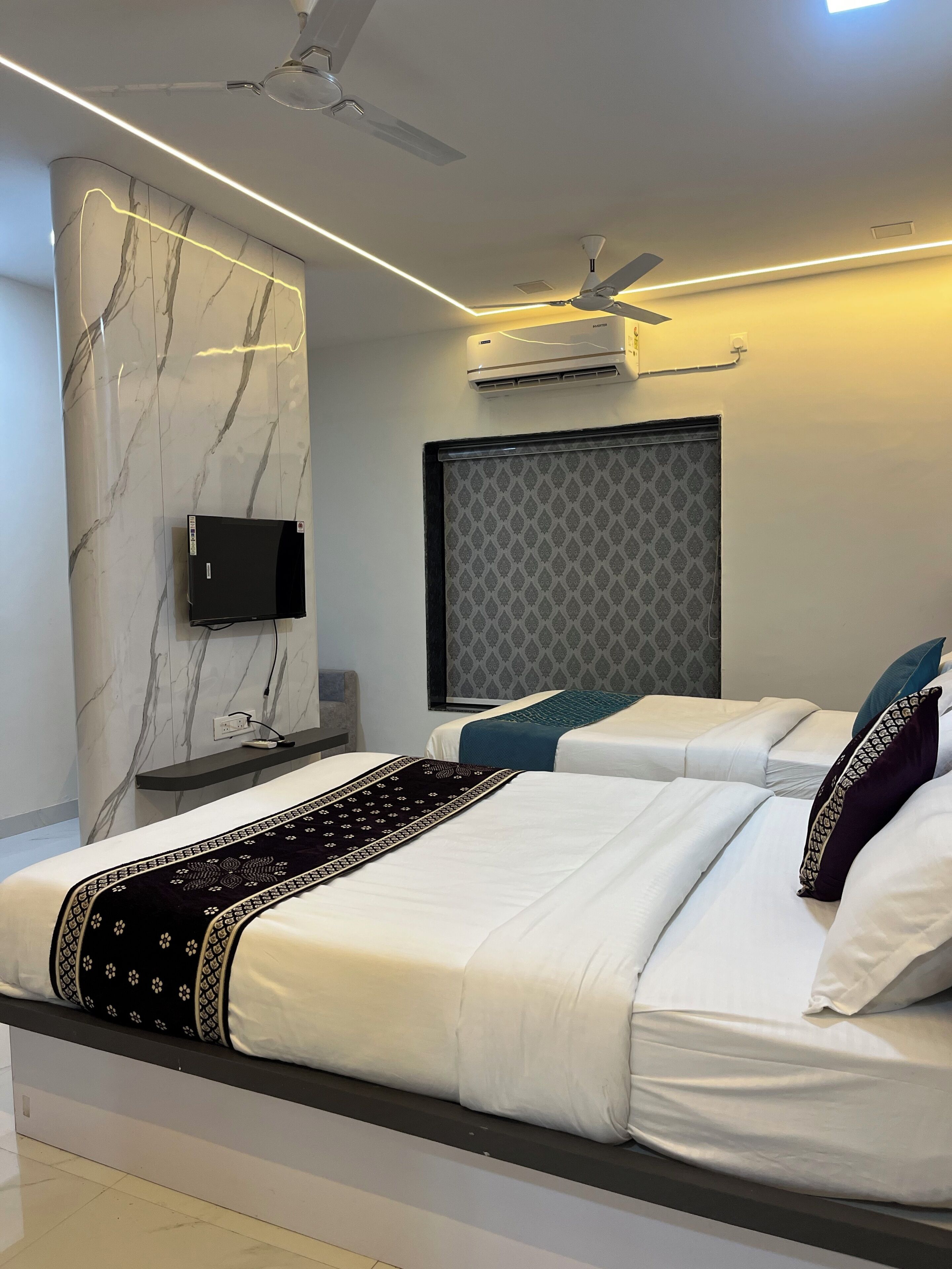 A modern hotel room with a marble wall, a flat-screen TV, two beds with white bedding, a ceiling fan, and an air conditioning unit.