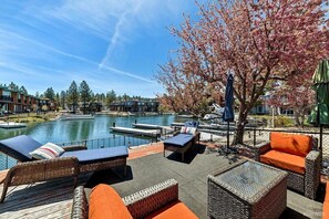 Eine Uferterrasse mit Korbmöbeln, Blick auf einen See, anlegende Boote und eine Reihe von Gebäuden im Hintergrund.