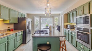 A modern kitchen with green cabinets, stainless steel appliances, a central island, and a pendant light. - Fabulous 5-bedroom house in Colorado Springs, perfect for relaxing (Colorado Springs)