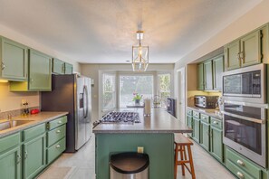 A modern kitchen with green cabinets, stainless steel appliances, a central island, and a pendant light. - Fabulous 5-bedroom house in Colorado Springs, perfect for relaxing (Colorado Springs)