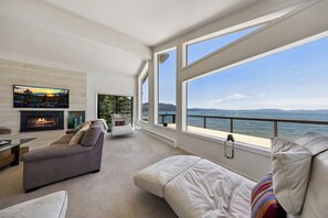 Uma sala de estar moderna com lareira, uma TV grande e vista para a água.