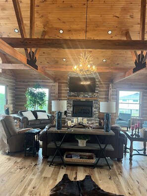 Ein Holzblockhaus-Interieur mit Kamin, Ledersofas, einer Kristallleuchter und einer Wand aus Naturstein.