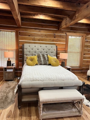 Un dormitorio de cabaña de madera con una cama grande, dos mesitas de noche y un banco.