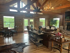 Ein Interieur einer Holzhütte mit Essbereich, Kamin, Ledersofa und Blick ins Freie.