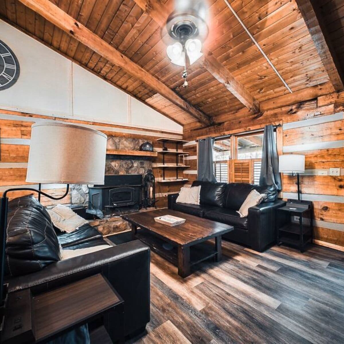 A log cabin interior with a fireplace, leather furniture, and wooden walls.