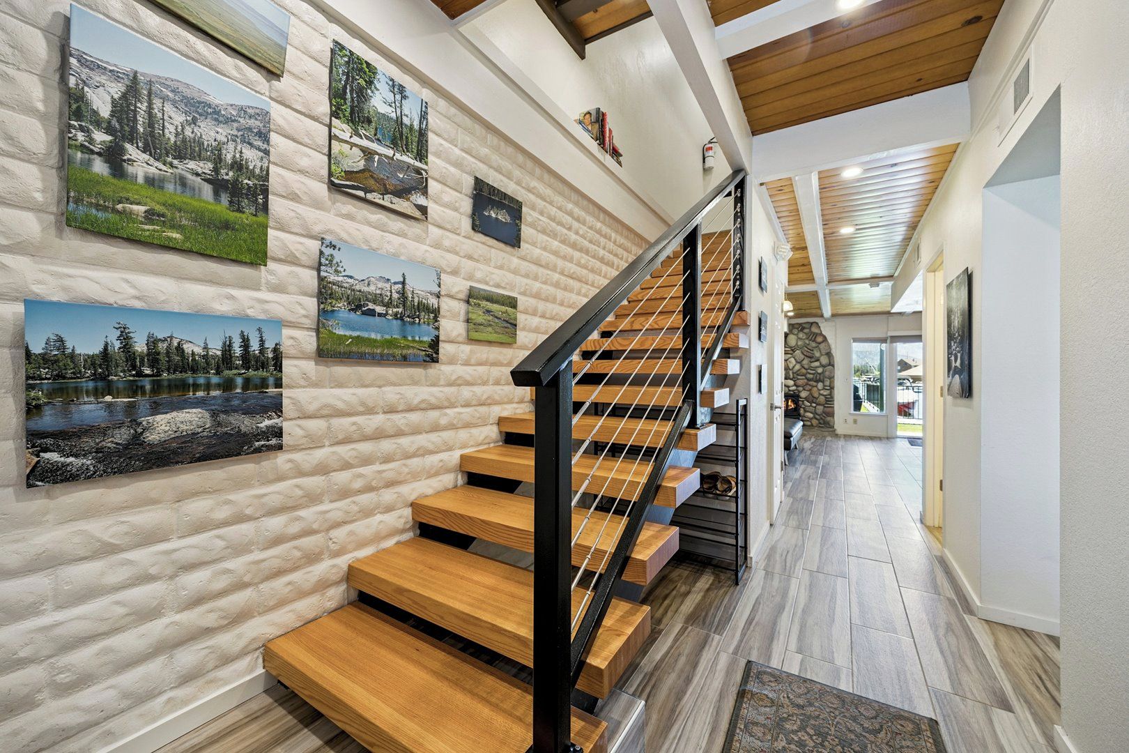 Una escalera de madera con barandilla metálica que conduce a una habitación con pared de piedra y cuadros enmarcados.