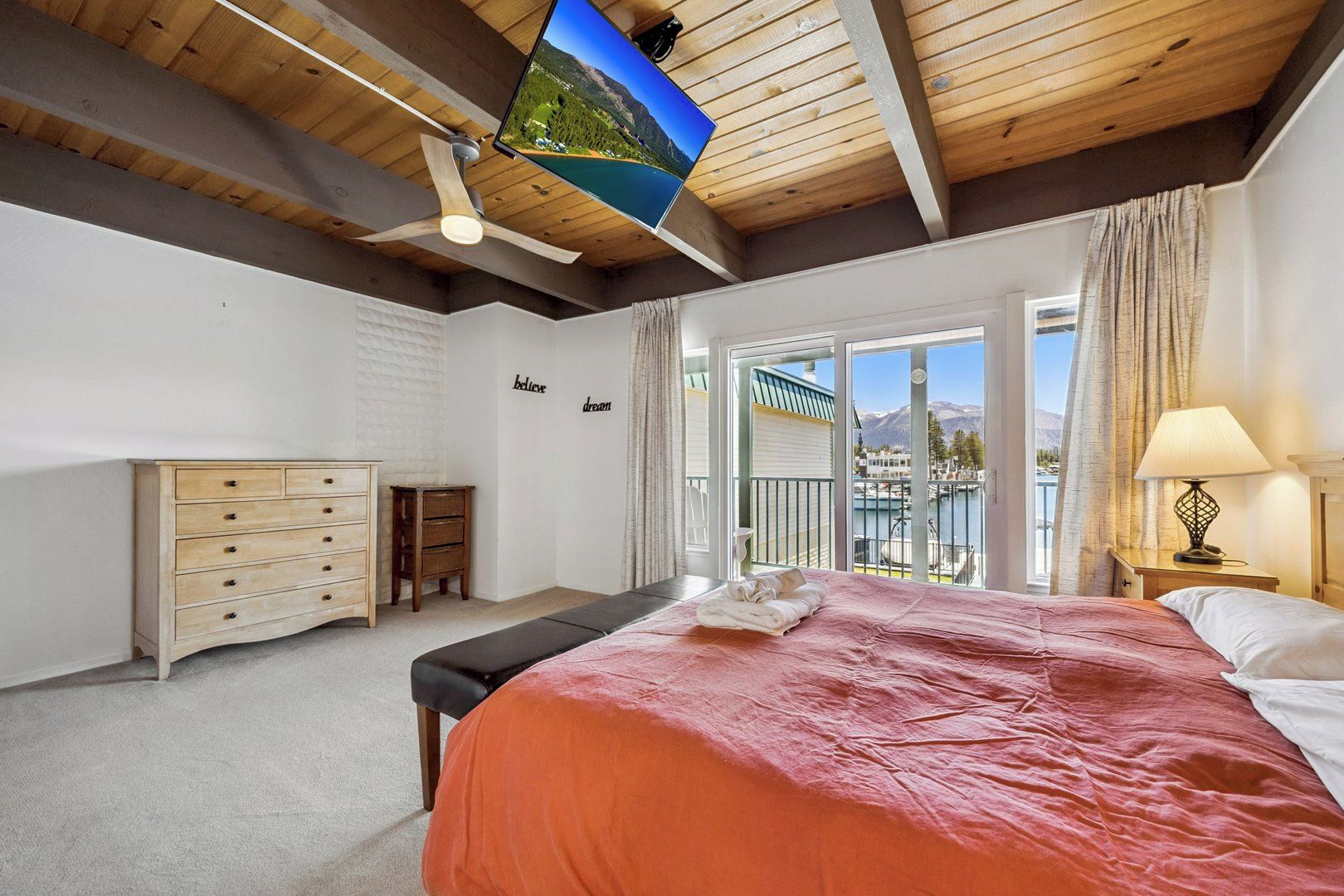 Une chambre à coucher comprenant un lit, une commode, un banc, un téléviseur et un balcon avec vue.