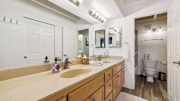 Une salle de bain avec un meuble-lavabo à deux vasques, un grand miroir avec éclairage intégré, des toilettes et un espace douche.