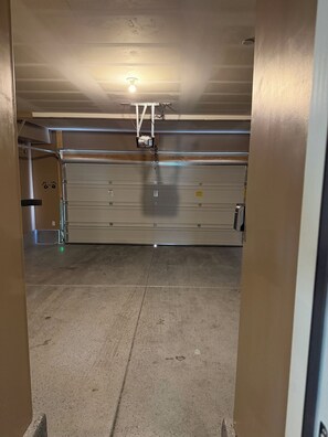 A parking garage with a closed garage door, a ceiling light, and a metal structure. - Cozy Townhome, 17 min to downtown & Nellis AFB (North Las Vegas)