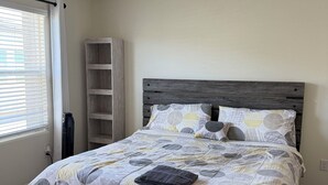 Un dormitorio con cama, mesita de noche, estantería empotrada y ventana con persianas.