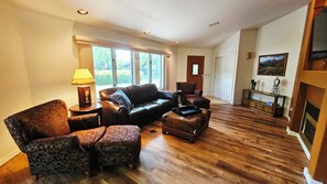 A spacious living room with a leather sofa, patterned armchairs, and a wooden floor.