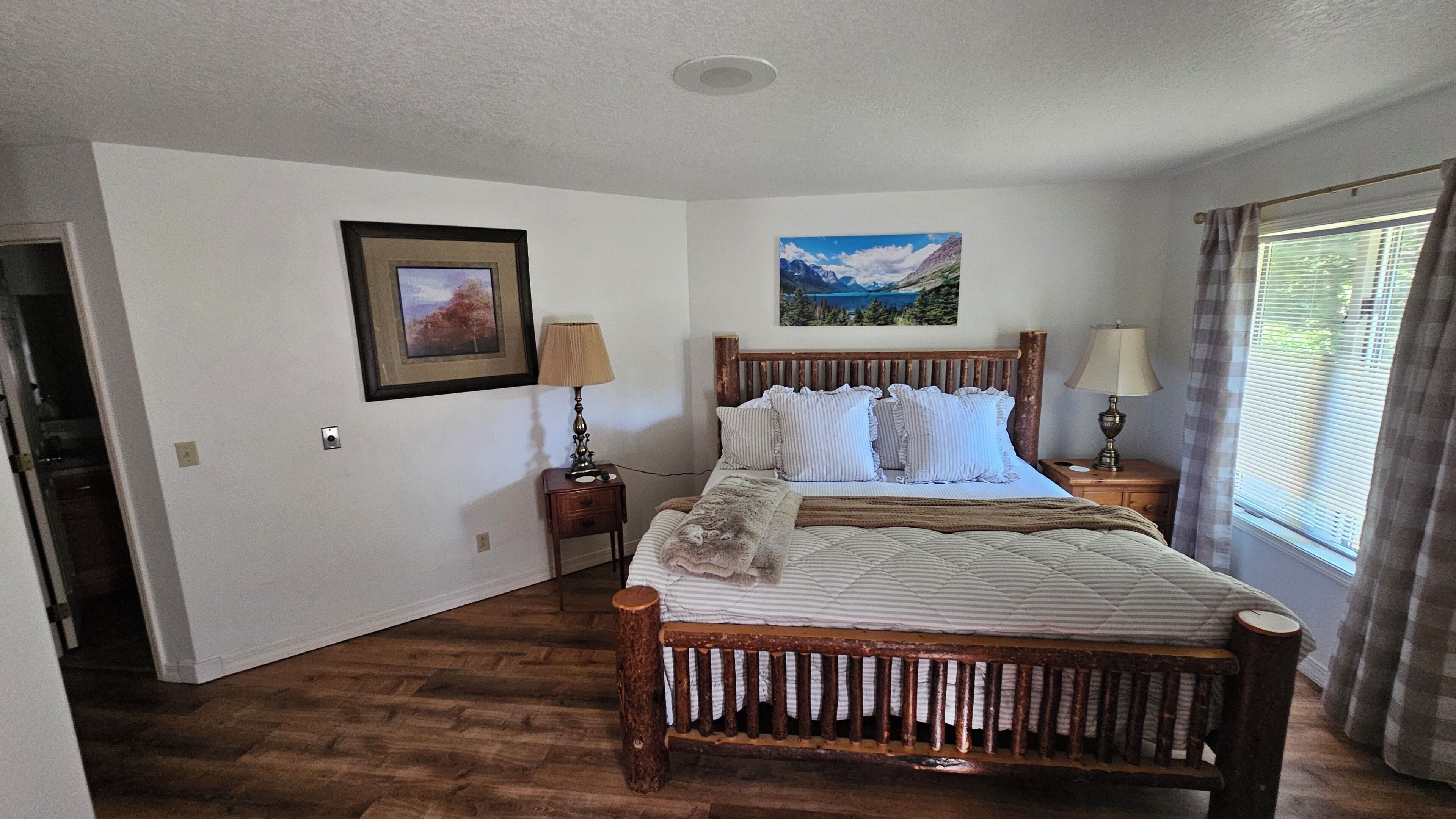 A bedroom with a wooden bed, a framed picture on the wall, and a window with curtains.