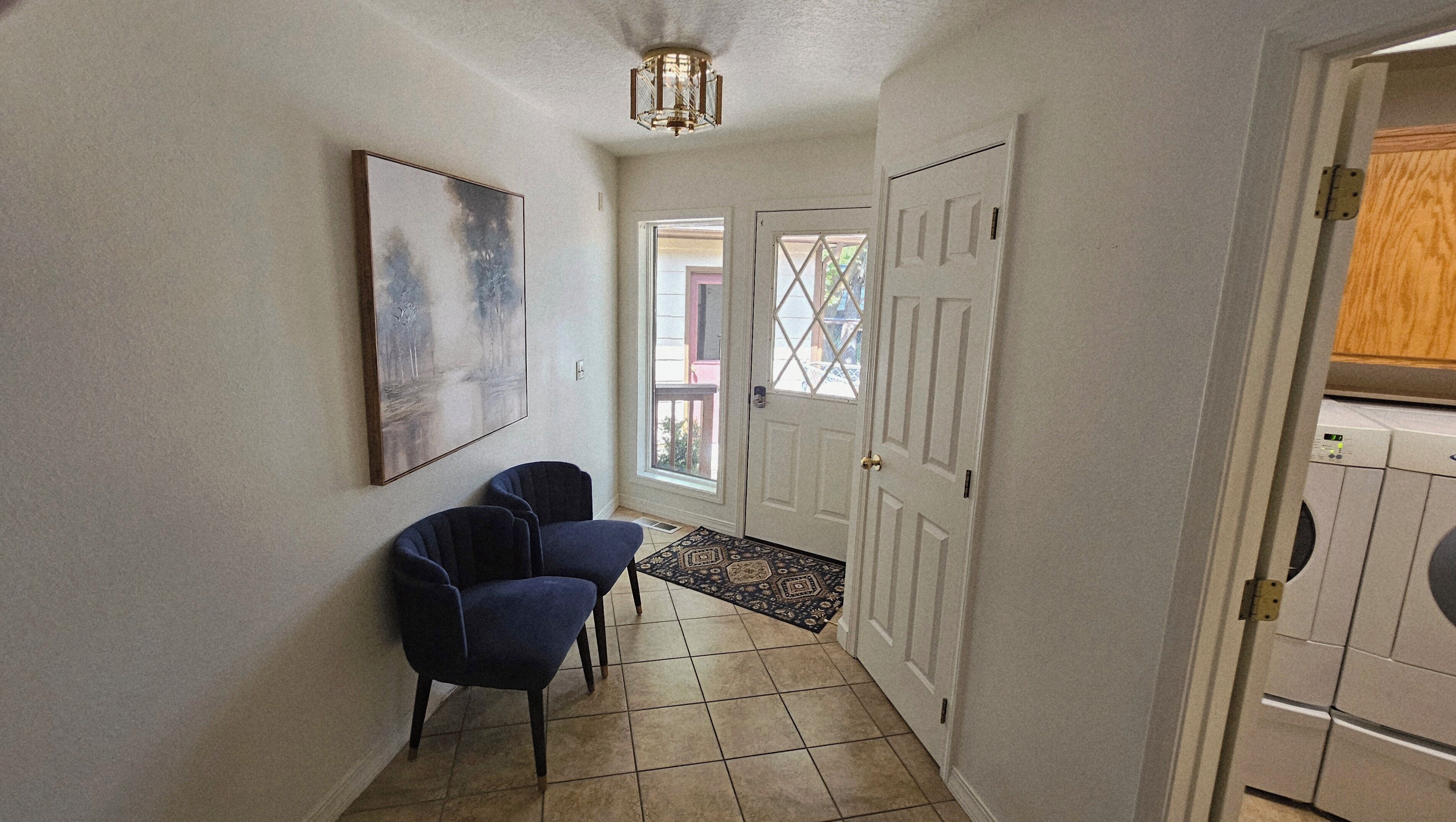 Un couloir avec une porte, une chaise, un tapis et un luminaire au plafond.
