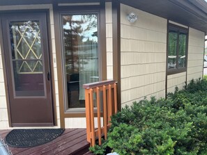 A house with a brown door, a sliding glass door, and a small porch with a wooden railing.