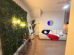 A living room with a green wall, a sofa with a Texas flag, a mirror, and a small table with a plant. - Rooftop Retreat Near Lower Greenville & Downtown (Dallas)