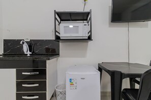 Eine kleine Küchenzeile mit einer Mikrowelle, einem Kühlschrank, einer Spüle und einer schwarzen Arbeitsplatte.
