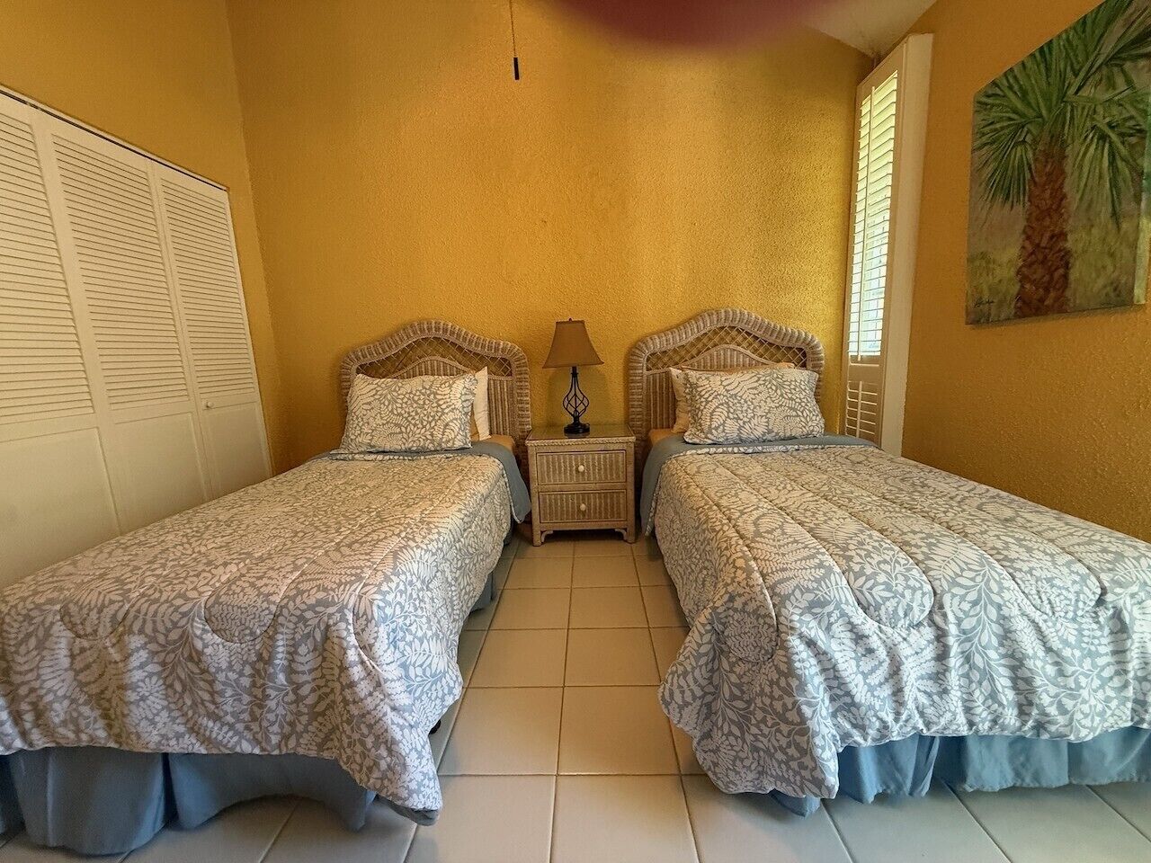 A bedroom with two beds, a nightstand, a lamp, and a window with blinds.