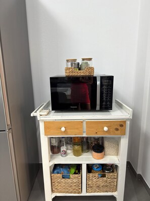 A kitchen area with a microwave, a small cabinet with drawers, and wicker baskets containing jars and bottles.