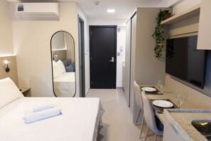 Ett hotellrum med en säng, ett litet skrivbord med en stol, en spegel, en dörr och en tv.