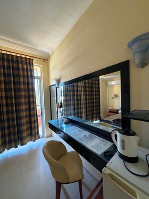 A hotel room with a desk, chair, and a coffee maker.