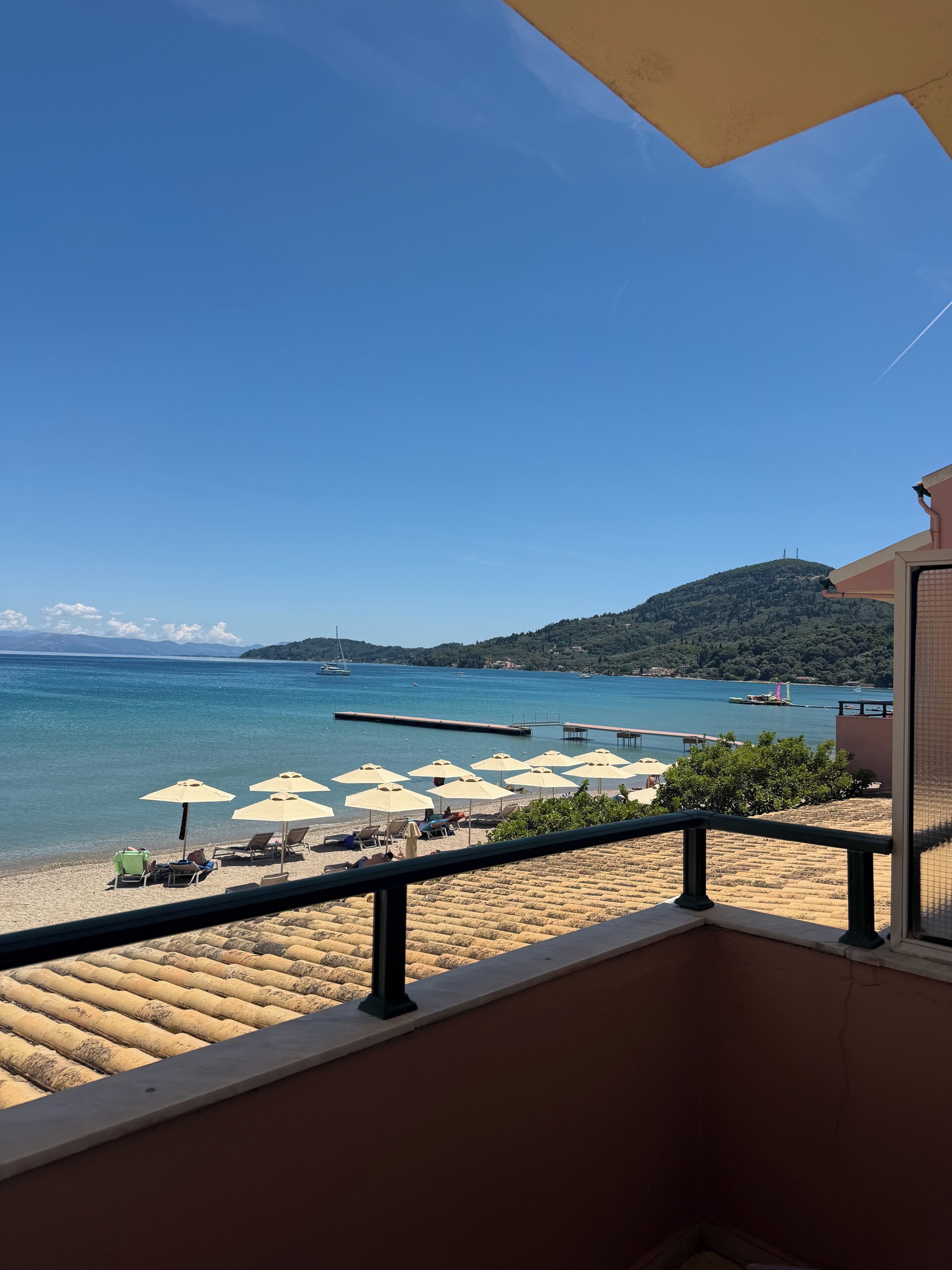 A balcony with a view of a beach, umbrellas, and a pier.
