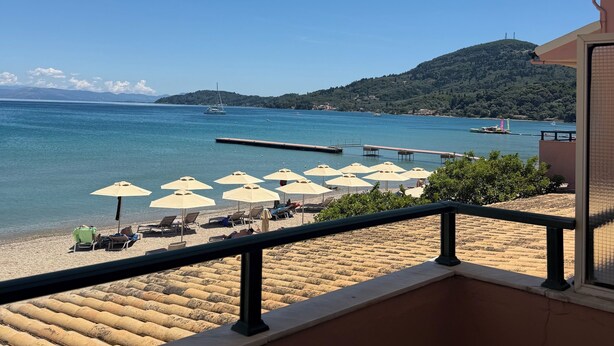 A balcony with a view of a beach, umbrellas, and a pier. - Messonghi Blue Bay  (Messonghi)