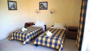 A hotel room with two beds, each with a checkered bedspread, two wall-mounted lamps, and two framed pictures on the wall.