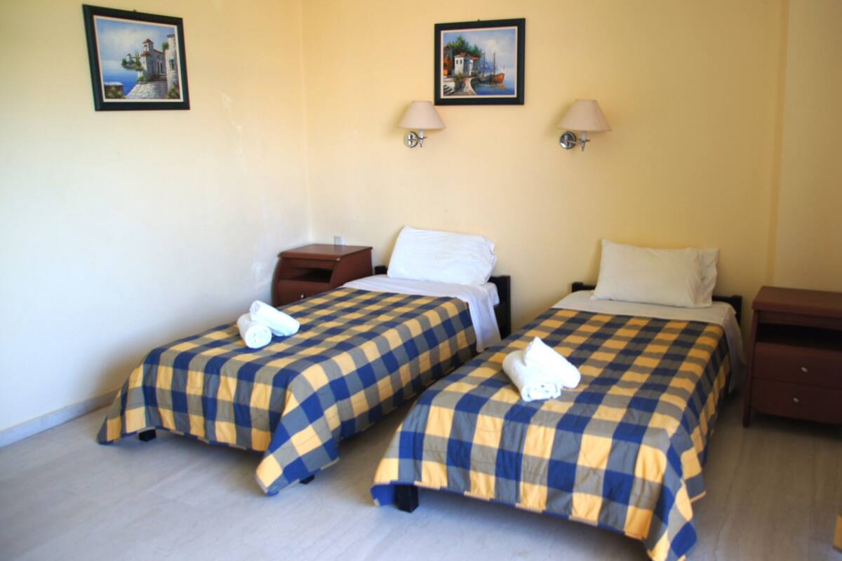 Habitación de hotel con dos camas, cada una con una colcha a cuadros, dos lámparas de pared y dos cuadros enmarcados.
