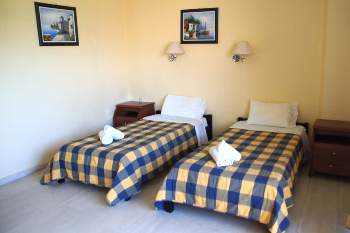 Une chambre d’hôtel avec deux lits, chacun recouvert d’une couvre-lit à carreaux, deux lampes fixées au mur et deux tableaux encadrés accrochés au mur.