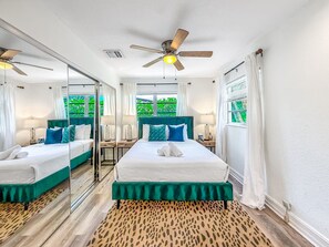 Ein Hotelzimmer mit zwei Betten, einem Deckenventilator, einem großen Spiegel und Blick auf Grünfläche.