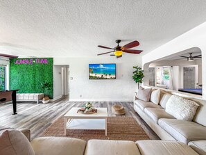 Ein modernes Wohnzimmer mit grüner Wand, Deckenventilator, Fernseher und Billardtisch.